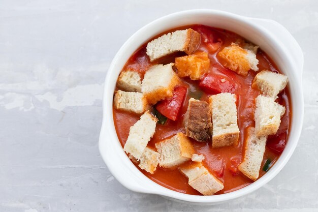 Cold tomato soup gaspacho with bread in white bowl on ceramic