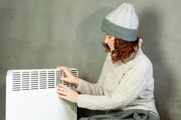 Photo cold winter in the apartment a girl warms her hands near the heater battery heating season energy