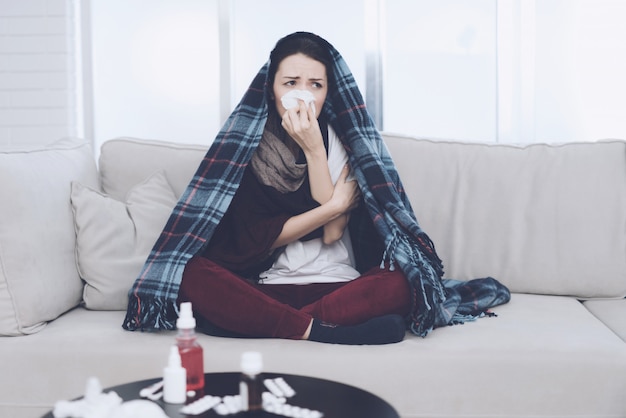 Cold woman sits on light couch wrapped in blue whip.