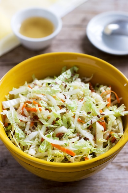 Coleslaw of cabbage, carrots and various herbs with mayonnaise in a large plate on a wooden surface