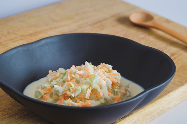 Coleslaw salad in black bowl on wood cutting board background.