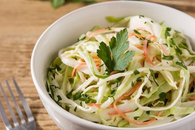 Coleslaw salad in white bowl on wooden table. Close up