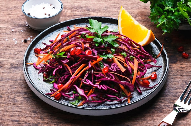 Coleslaw salad with red cabbage carrot parsley pomegranate seeds and orange olive oil dressing on wooden kitchen table background top view
