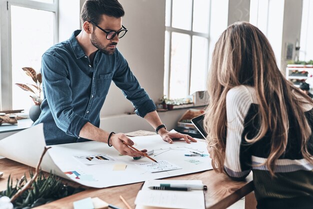 collaboration is a key to best results. two young modern people in smart casual wear using blueprint