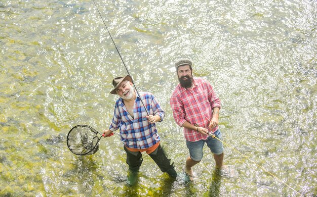 釣り竿とネットの父と息子の釣りとのコラボレーション2人の幸せな漁師湖のほとりでの密猟キャンプ田舎の逃走趣味の野生の自然の大物釣り友情の概念