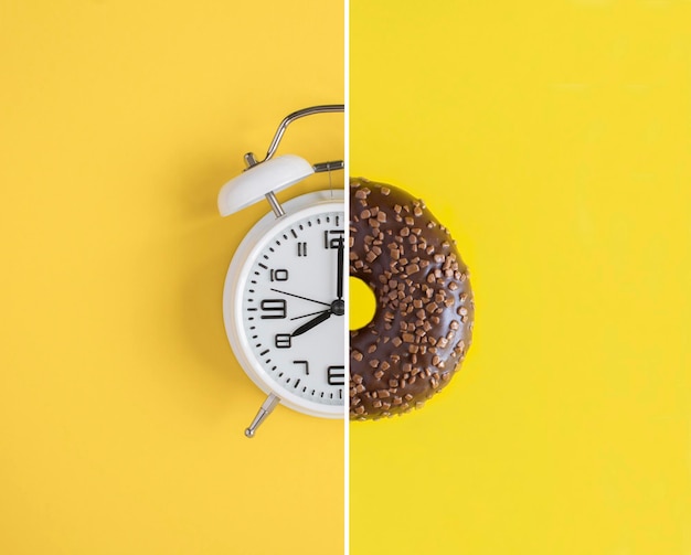 Collage of white alarm clock and donut with chocolate glaze on the yellow background Copy space Closeup