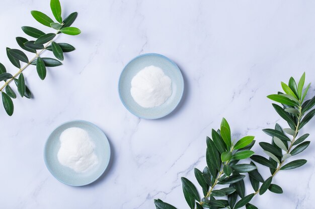 Collageenpoeder op een trendy marmeren ondergrond met groene olijfboombladeren. Natuurlijke schoonheid en gezondheidssupplement, wellness skincare anti-aging concept. Bovenaanzicht, plat leggen, ruimte kopiëren