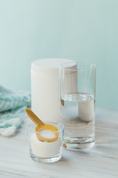 Collagen powder in bowl, glass of water and measure spoon on a on light blue background. Extra protein intake. Natural beauty and health supplement concept.