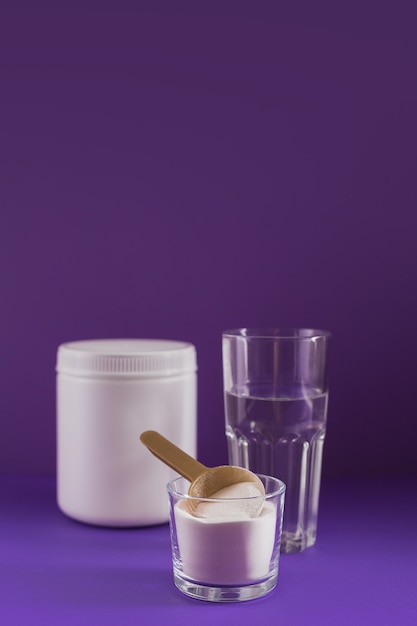 Collagen powder in bowl, glass of water and measure spoon on purple