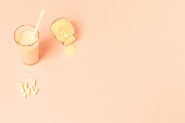 Collagen powder, milk and pills on pink background.