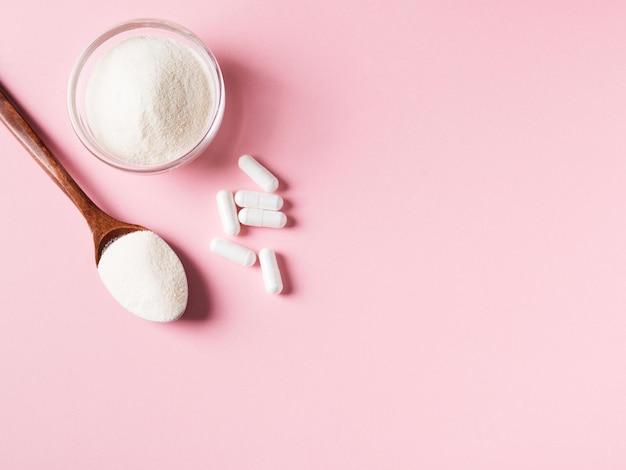 Collagen powder spoon and pill or capsule supplement healthy and anti age concept flat lay on pink background
