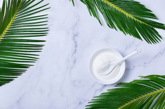 Collagen powder on a trendy marble background with green palm leaves. Natural beauty and health supplement, wellness skincare anti-aging concept. Top view, flat lay, copy space