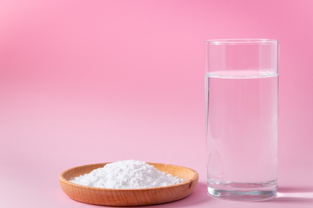 Collagen powder in wooden bowl and glass of water on pink background Biological natural protein