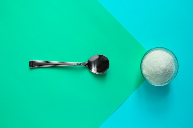 Photo collagen protein powder in jar and spoon on green table.