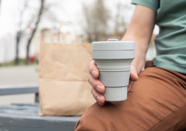 持ち帰り用のコーヒーや紅茶用の折りたたみ式エコカップ。持続可能なシリコンマグカップを持つ男性の手。ゼロウェイストライフスタイル。