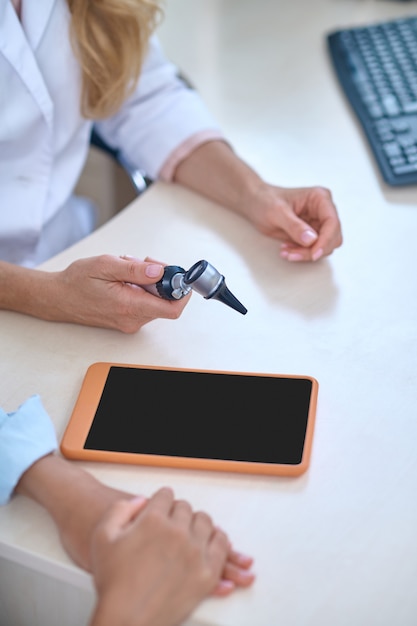 Colleagues, doctors. Hands of doctor otolaryngologist in white coat sitting at table with tablet communicating with patient, no face