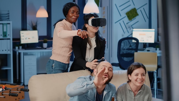 Colleagues enjoying video games with vr glasses and joystick to celebrate with drinks after work. Workmates using headset with virtual reality to play game after hours. Workers playing