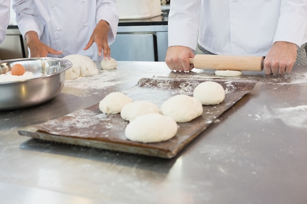 Colleagues kneading dough with rolling pin