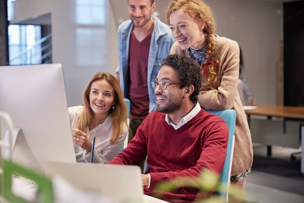 Photo colleagues looking over shoulder of young man working in modern office