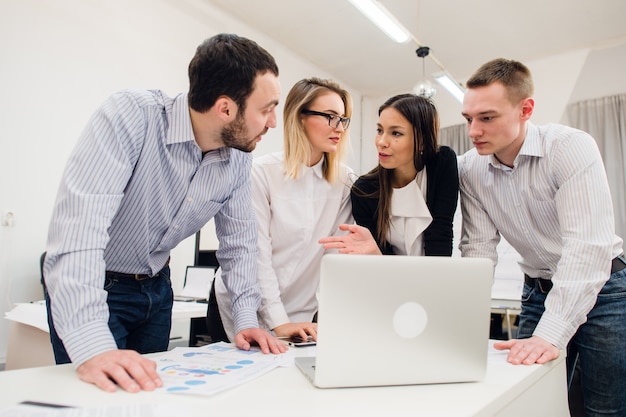 Colleagues at an office talking and working on a laptop