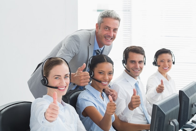 Colleagues with headsets using computers while gesturing thumbs up