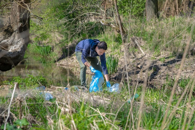 Foto raccogliendo i rifiuti in un sacchetto di plastica, un volontario aiuta nella foresta sulla riva del fiume