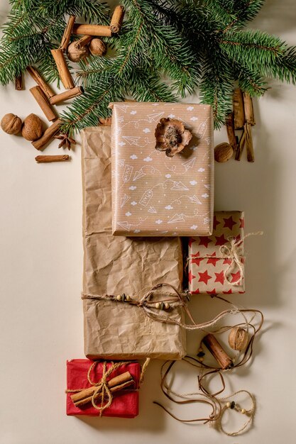 Collection of Christmas gift boxes in eco-friendly recycled craft paper decorated by natural nuts and cinnamon sticks over beige paper background with fir tree branches. Eco xmas gifts. Flat lay