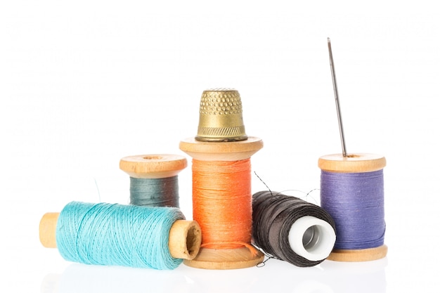 Collection of color thread spools with needle and thimble isolated on white .