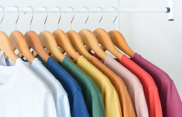 collection of colorful tshirts hanging on wooden clothes hangers over white background