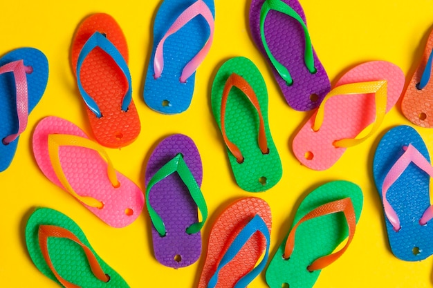 Collection of colourful summer flip flop sandals on a bright yellow background