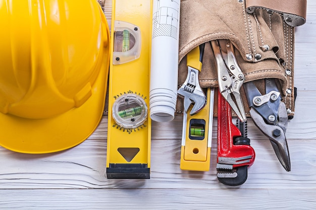 Collection of construction tooling leather tool belt blueprints building helmet on wooden board.