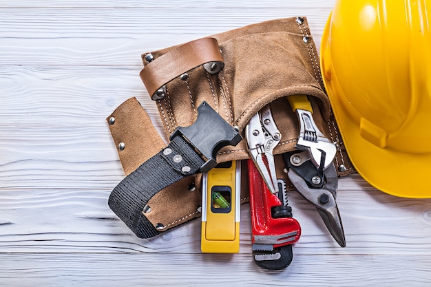 Collection of construction tooling in leather tool belt safety building helmet on wooden board