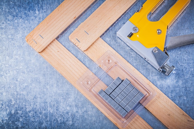 Collection of stapler gun metal staples wooden building board on metallic background