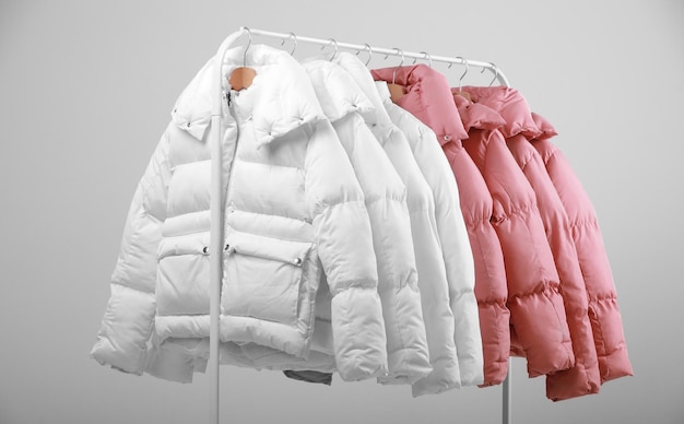 Collection of stylish white and soft pink colours warm jackets\
hanging on wooden clothes hanger on metal clothing rack on white\
background new autumnwinter fashion collection in store copy\
space