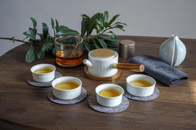 A collection of tea cups on a table with a glass of whiskey and a cup of tea.