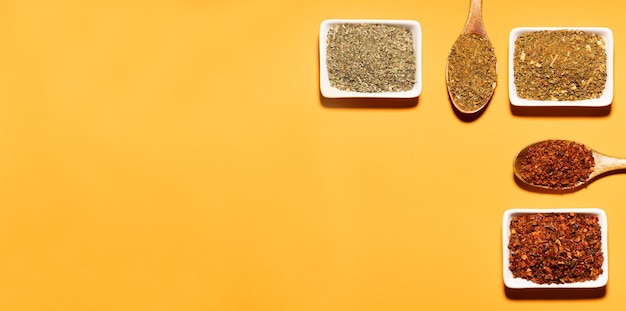 Collection of three spices on wooden spoons and white bowls on orange background