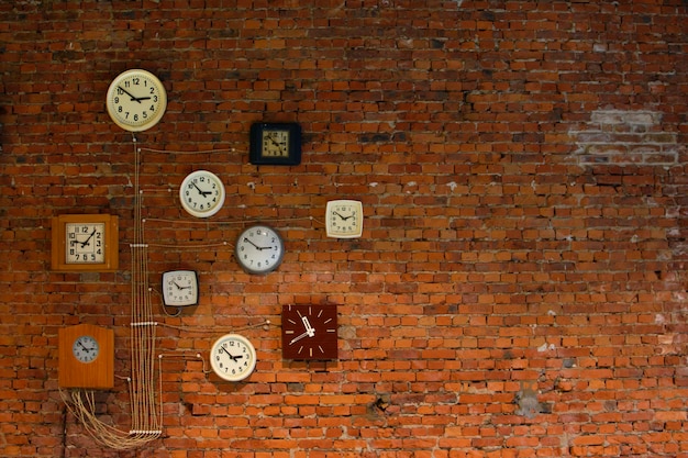 Collection of vintage wall clocks hanging on an old brick wall.