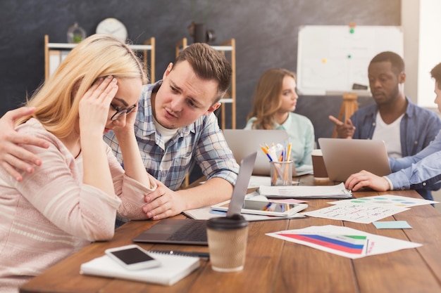 Collega die Kaukasisch ondersteunt bij het lezen van slecht nieuws in e-mail, het troosten van een gestresste vrouwelijke collega met hoofdpijn, van streek door ontslag, het helpen oplossen van een probleem op kantoor