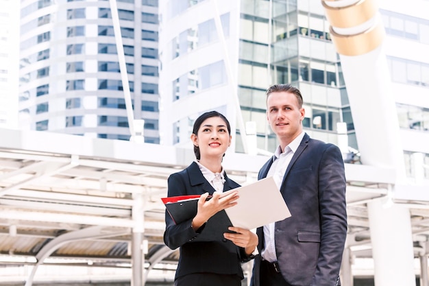 Collega met map die naar boven kijkt terwijl hij tegen een gebouw in de stad staat