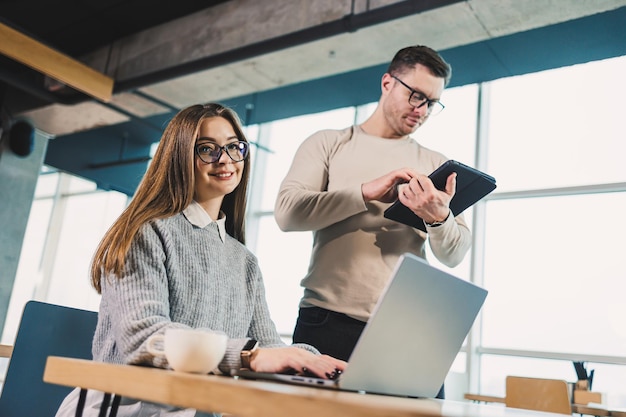 Collega's communiceren tijdens het werken met een laptop in het kantoor Twee werknemers in een moderne werkruimte Twee jonge zakenlieden zitten samen aan een tafel