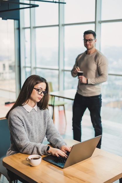 Collega's communiceren tijdens het werken met een laptop in het kantoor Twee werknemers in een moderne werkruimte Twee jonge zakenlieden zitten samen aan een tafel