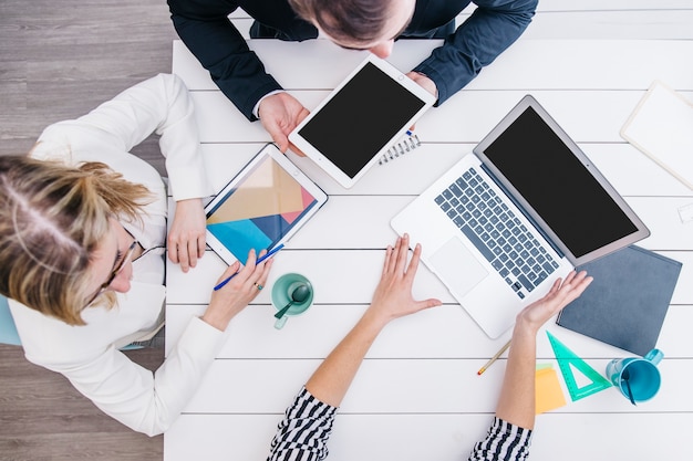 Foto collega's die gadgets gebruiken bij bureau