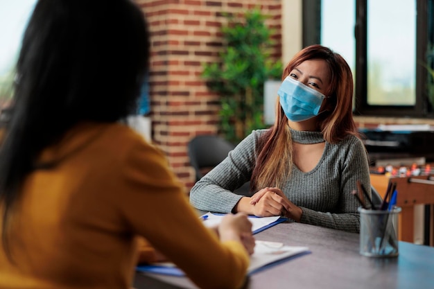 Collega's die marketingstrategie bespreken die bedrijfsgrafieken analyseren die werken bij zakelijk partnerschap in startup-kantoor. Zakenvrouwen die een medisch gezichtsmasker dragen om infectie met covid te voorkomen