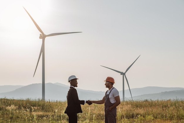 Collega's handen schudden met windturbines op de achtergrond