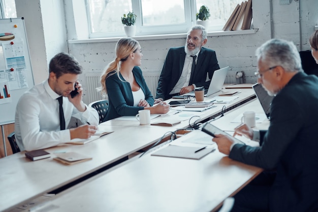 Collega's in elegante formele kleding die moderne technologieën gebruiken terwijl ze op kantoor werken