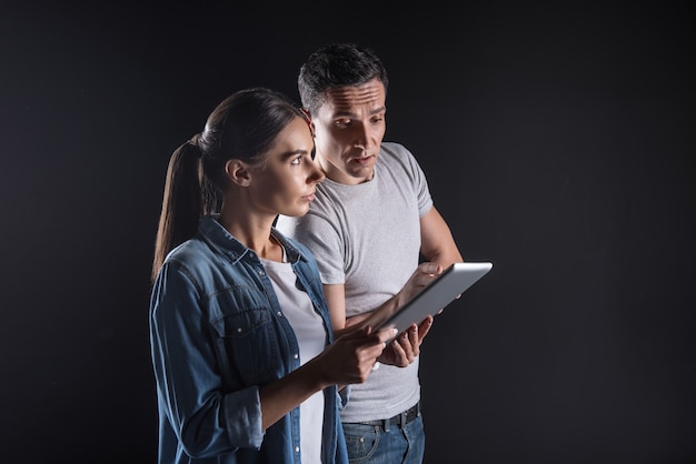 Collega's op het werk. Slimme mooie jonge vrouw die een tablet houdt en naar het digitale scherm kijkt terwijl hij naar de monitor kijkt