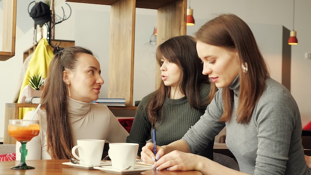 Collega's-vrouwen bespreken gezamenlijk project in café in het coworking-centrum en maken aantekeningen in een notitieboekje.