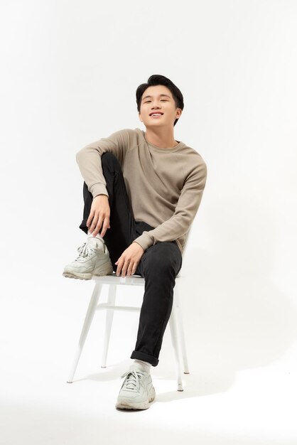 College age man sitting on a white chair isolated on white