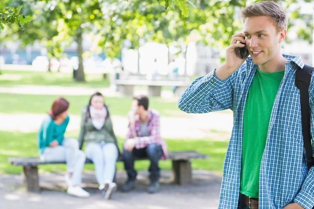 Photo college boy using cellphone with blurred students in park