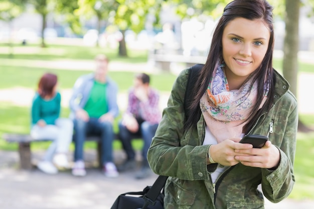 Колледж девушка текстовых сообщений с размытыми учениками в парке